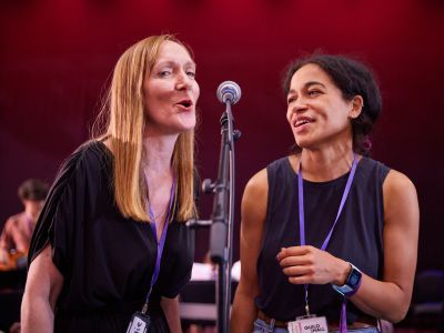 Two women sharing a microphone, smiling and singing together